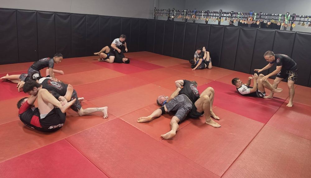 Adults rolling during a No Gi class